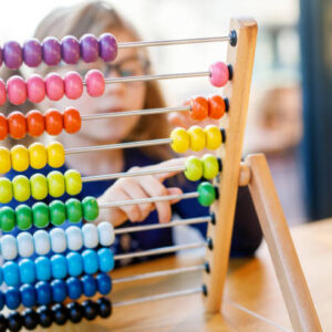 Little preschool girl playing with educational wooden rainbow toy counter abacus. Healthy happy child with glasses learning to count and colors, indoors on sunny day